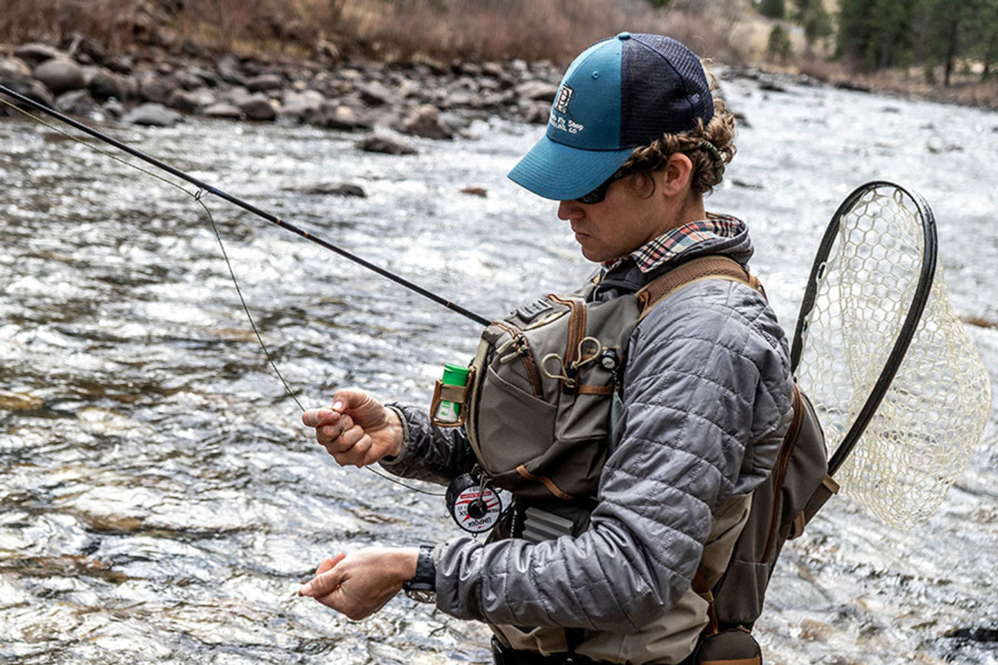 Person fly fishing in a river wearing a backpack and cap.